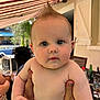 baby, child, mohaawk, hair, drool, face, skin, hands, outdoor, patio, awning, furniture, person, holding, curious, expression, daylight, window, glass, table