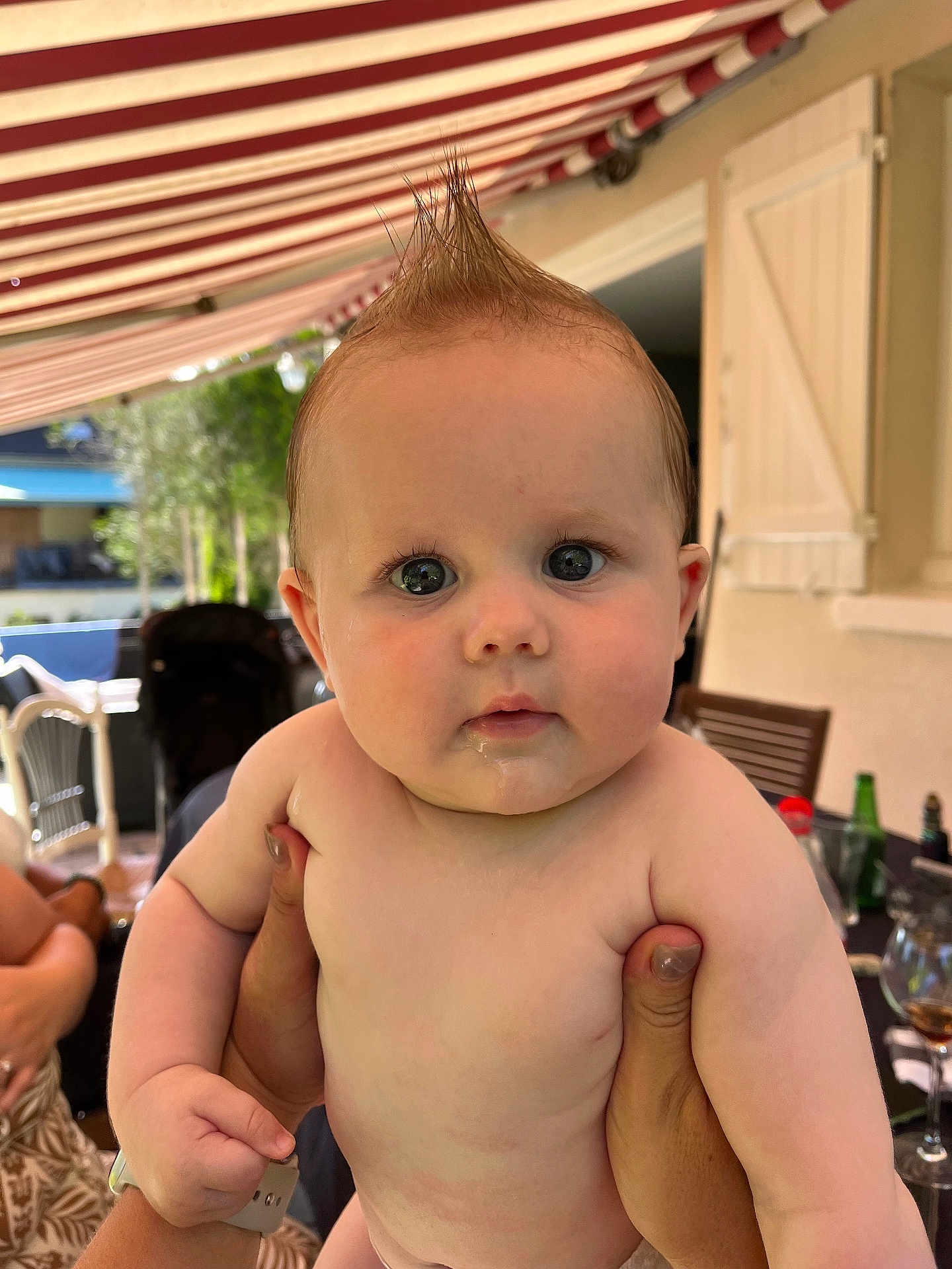 Lony a rejoint le concours — aidez-le/la à gagner de superbes lots ! baby, child, mohaawk, hair, drool, face, skin, hands, outdoor, patio, awning, furniture, person, holding, curious, expression, daylight, window, glass, table
