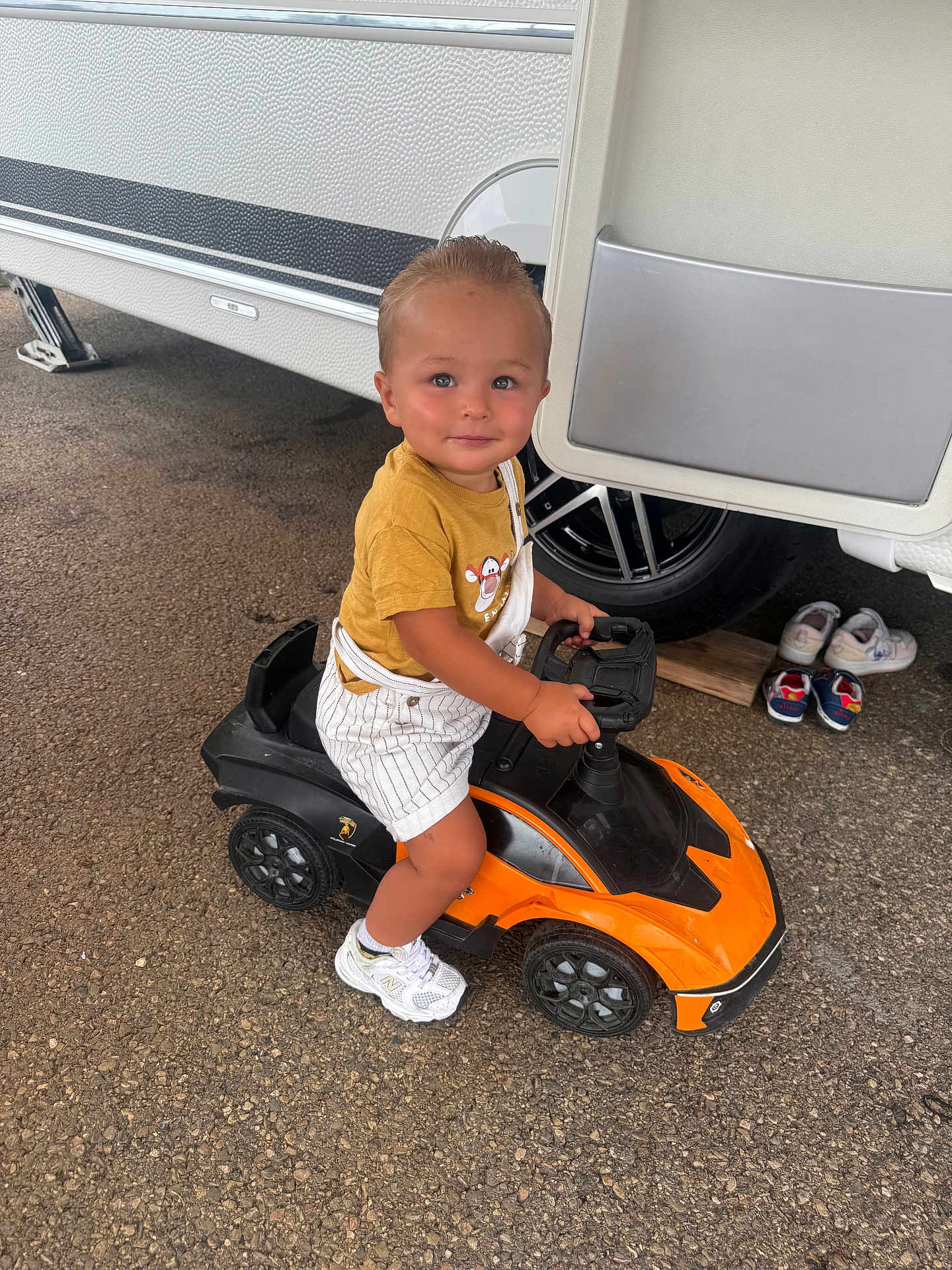 Taysem participe au concours pour gagner de l'argent avec cette photo : toddler, child, toy_car, orange, black, yellow_shirt, striped_overalls, white_shoes, gravel, trailer, wheel, outdoor, smiling, cute, person, small_shoes, play, vehicle, ground, daylight