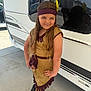 child, girl, costume, headband, feather, long_hair, brown_hair, posing, boots, outdoor, vehicle, reflection, concrete, smiling, hand_on_hip, dress, sunlight, casual, portrait, young_person