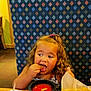 basket, booth, casual, child, chip, cup, curious, curly_hair, drink, eating, food, indoor, meal, patterned_background, restaurant, salsa, snack, straw, table, toddler