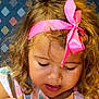 child, clothing, colorful, curly_hair, cute, expression, face, focused, hair, headband, indoor, patterned_background, pen, person, pink_bow, portrait, skin, striped_shirt, toddler, young_child