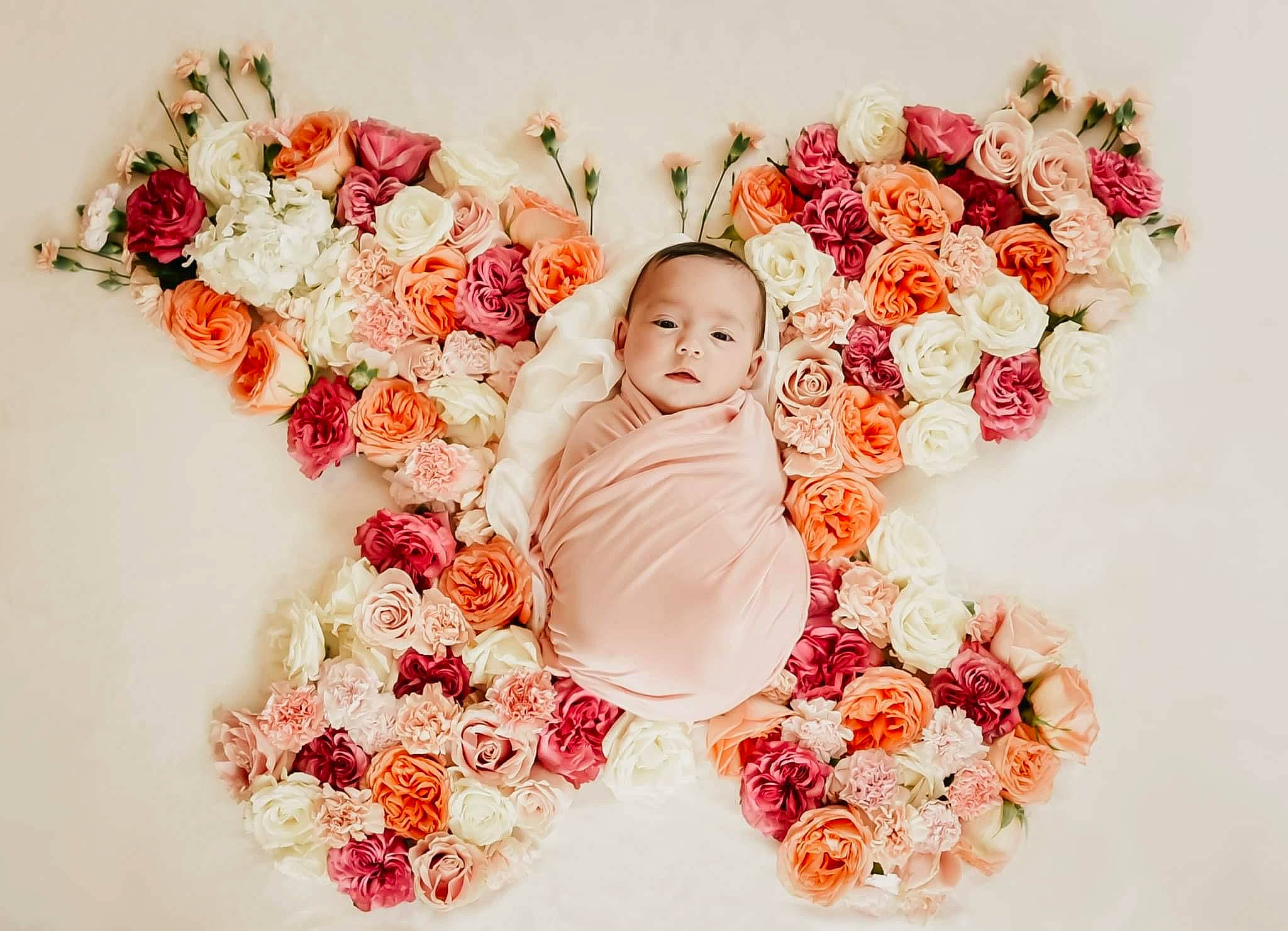 Kara is registered to the contest to win money with this photo: artificial_flower, baby, baby_toddler_clothing, bouquet, flower, flower_arranging, flowering_plant, garden_roses, happy, headpiece, human_body, hybrid_tea_rose, orange, person, petal, pink, plant, red, rose, textile