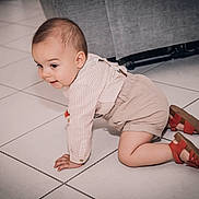 Lëlyo a rejoint le concours — aidez-le/la à gagner de superbes lots ! baby, beige_shorts, child, clothing, couch, crawling, curious, face, floor, footwear, hands, head, home_interior, indoors, knees, long_sleeve_shirt, person, red_sandals, tile_floor, young_child