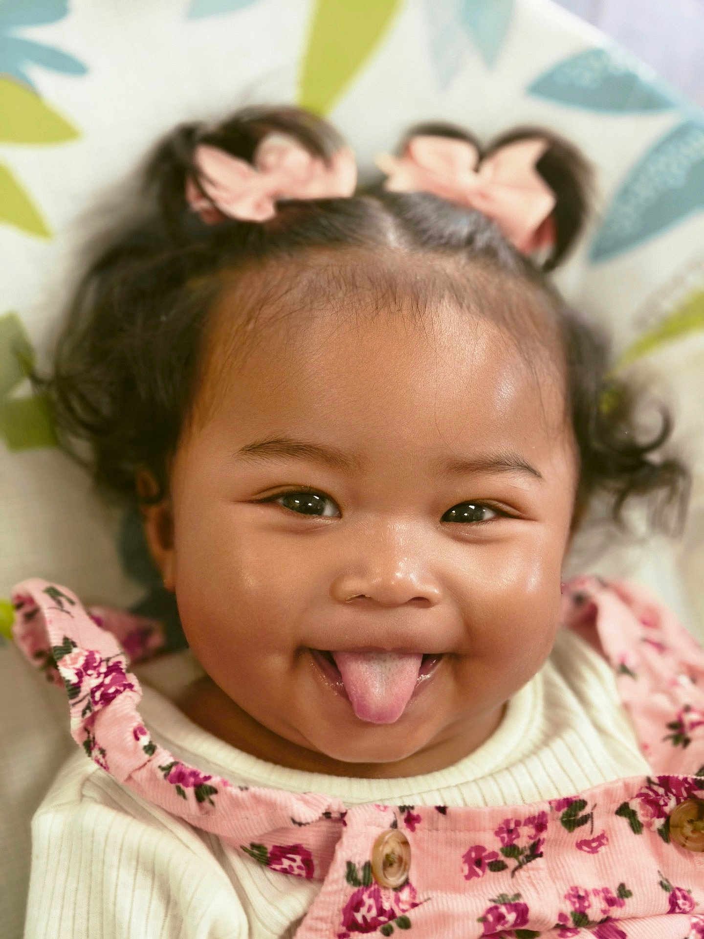 Elodie joined the competition — help win amazing prizes! baby, child, tongue_out, pink_bows, pony_tail, floral_dress, smiling, cute, face, portrait, happy, infant, clothing, patterned_background, close_up, skin, person, cheeks, sitting, playful