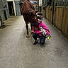 person, dog, horse, stable, barn, animal, pet, crouching, hugging, leash, stall, wooden, floor, indoor, barn_door, pink_jacket, black_pants, animal_care, friendly, companionship