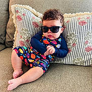 Adriel joined the competition — help win amazing prizes! baby, barefoot, casual, child, colorful_clothing, couch, cozy, curly_hair, cute, fashion, fish_pattern, home, indoor, infant, person, pillow, portrait, relaxed, seated, sunglasses