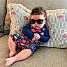 baby, barefoot, casual, child, colorful_clothing, couch, cozy, curly_hair, cute, fashion, fish_pattern, home, indoor, infant, person, pillow, portrait, relaxed, seated, sunglasses