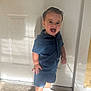 toddler, child, smiling, blue_clothing, shorts, shirt, white_sneakers, standing, indoor, door, carpet, shadow, happy, portrait, cute, young_child, person, casual_wear, light, expression
