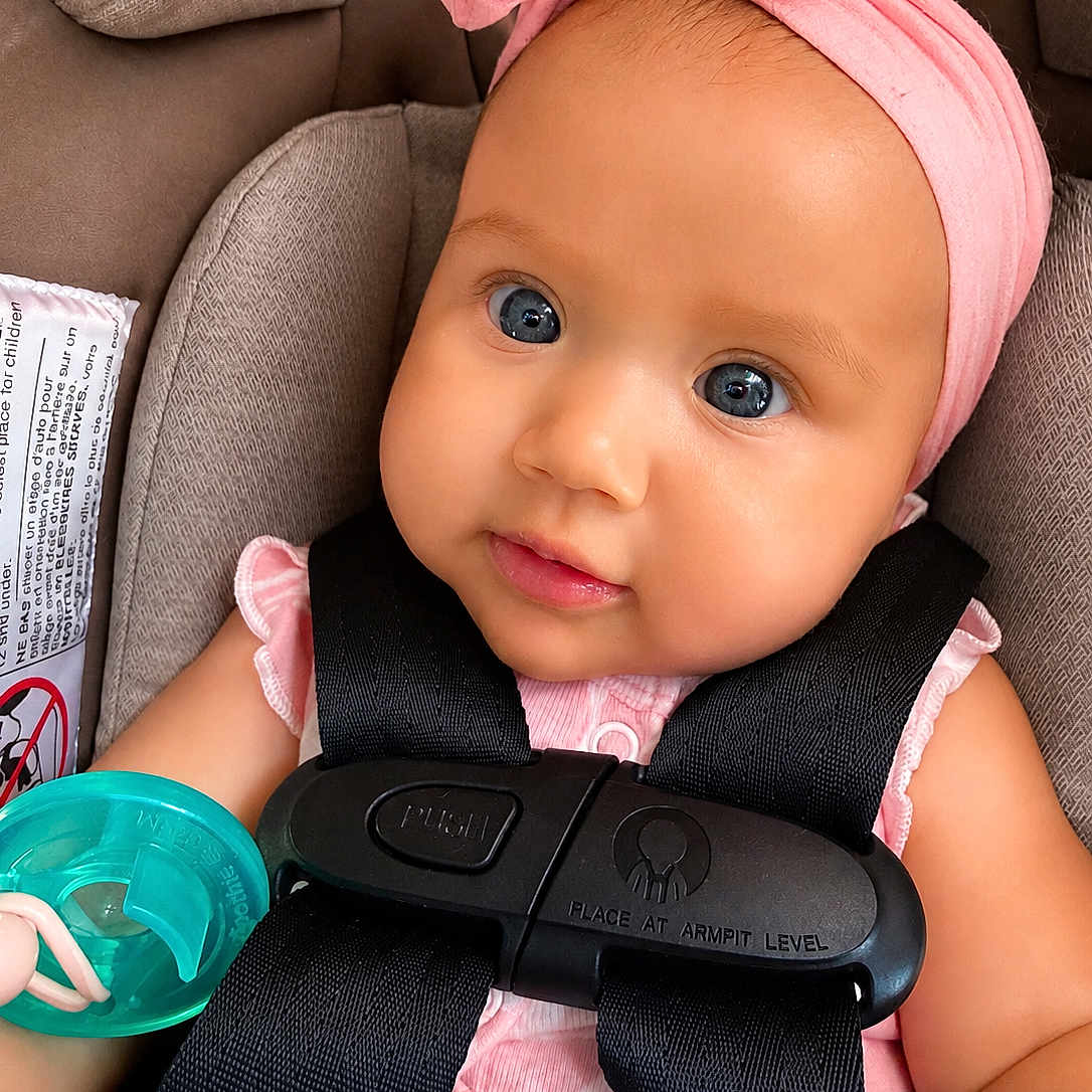 Gracia is registered to the contest to win money with this photo: baby, infant, car_seat, pacifier, pink_headband, blue_eyes, child, seatbelt, cute, closeup, face, straps, clothing, sitting, portrait, young_child, indoor, safety, adorable, infancy