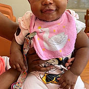 Khyla is registered to the contest to win money with this photo: baby, child, infant, pink_bib, swan, smile, pigtails, indoor, person, hand, lap, clothing, cute, young_child, seated, pacifier_clip, shorts, skin, cheeky, happy