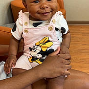 Khyla joined the competition — help win amazing prizes! baby, child, curly_hair, cute, face, hand, happy, indoor, infant, lap, minnie_mouse, orange_chair, person, pink_overalls, portrait, seated, skin, smiling, socks, wood_floor