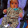 baby, infant, child, car_seat, pacifier, bow, leopard_print, animal_print, purple_cushion, sitting, portrait, wide_eyes, indoor, vehicle, safety_harness, fashion, blurred_hand, black_background, timestamp, smiling