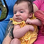 baby, infant, yellow_outfit, tattoo, arm, pink_shirt, blue_chair, outdoor, grass, person, skin, face, hand, leg, clothing, seated, holding, casual, relaxed, expression