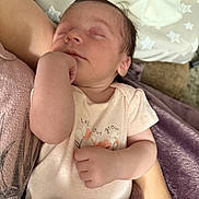 Lainey is registered to the contest to win money with this photo: baby, newborn, sleeping, infant, arm, onesie, flower, text, blanket, purple, skin, person, rest, cozy, comfort, cute, toddler, soft, bed, peaceful