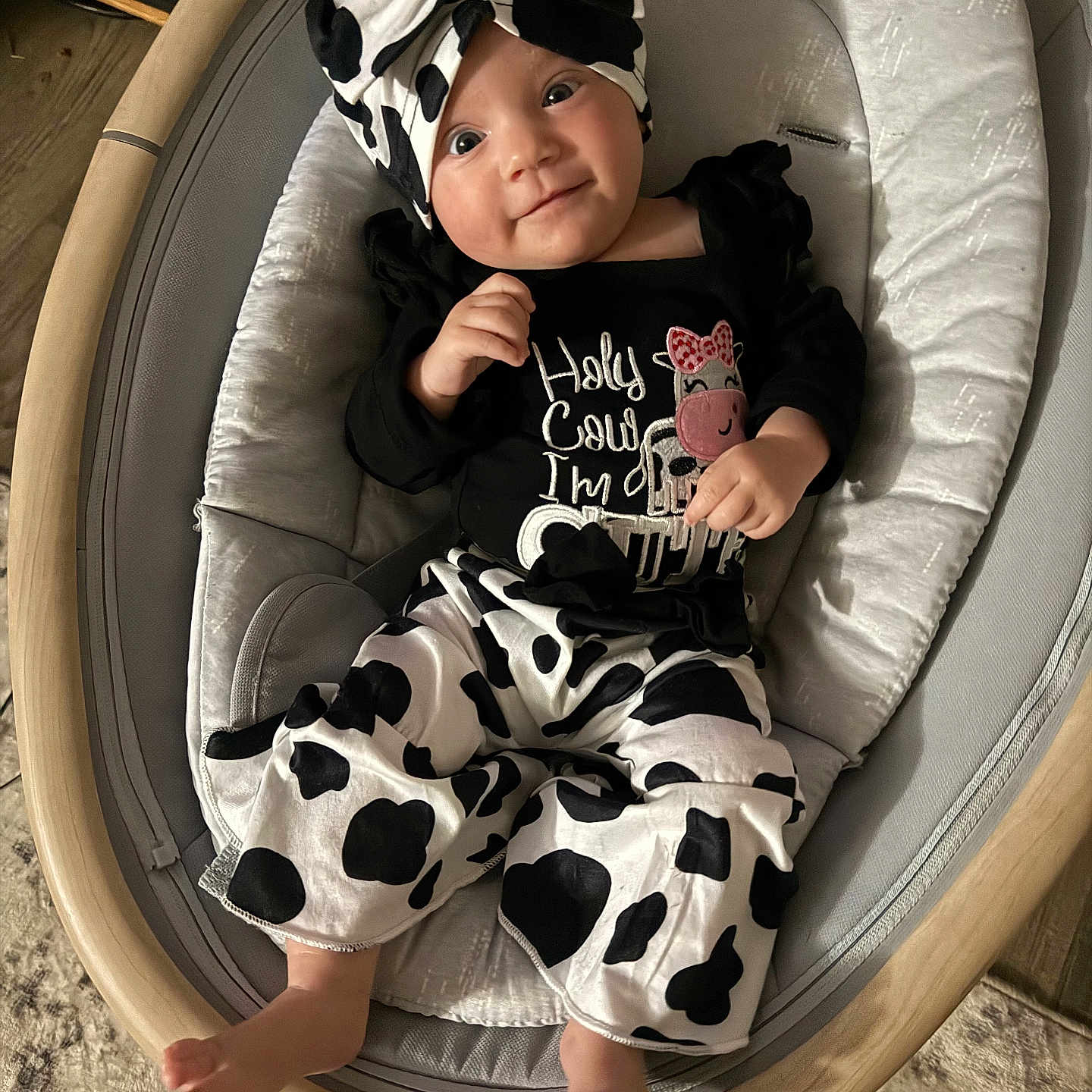 Lainey is registered to the contest to win money with this photo: baby, baby_clothes, baby_seat, black_and_white, bow, child, clothing, cow_print, cute, fabric, footwear, happy, headband, indoor, infant, person, portrait, sitting, smiling, wooden_frame
