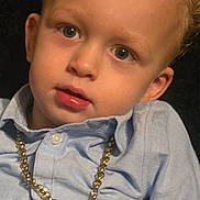 Lennon is registered to the contest to win money with this photo: child, portrait, face, curly_hair, blue_shirt, gold_chain, necklace, boxing_glove_pendant, young_child, closeup, expression, casual_clothing, fashion_accessory, indoor, person, cute, looking, curious, button_up_shirt, light_blue