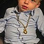 Lennon is registered to the contest to win money with this photo: toddler, child, boy, face, shirt, jeans, necklace, gold_chain, boxing_glove_pendant, casual_clothing, portrait, indoor, curly_hair, light_blue, dark_background, sitting, young_child, fashion_accessory, cute, expression