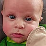 baby, infant, child, portrait, close_up, face, eyes, blue_eyes, serious, looking_at_camera, green_clothing, cushion, chair, indoor, patterned_background, head, skin, photography, sitting, adorable