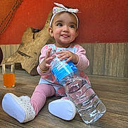 Ayra joined the competition — help win amazing prizes! baby, bow, child, cute, floor, girl, glass, headband, indoor, infant, orange_juice, pink_clothing, playful, shoes, sitting, smiling, tongue_out, wall, water_bottle, wooden_floor
