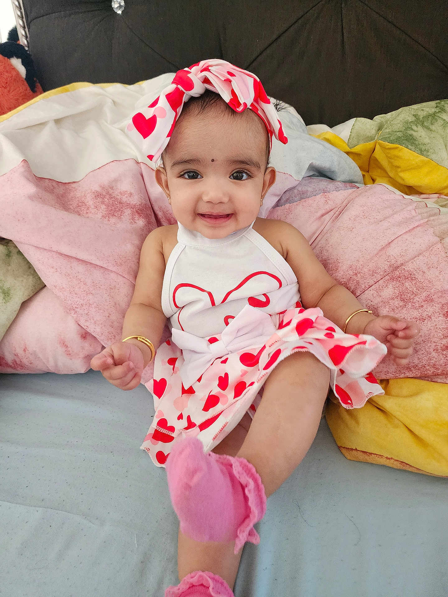 Ayra is registered to the contest to win money with this photo: baby, child, smiling, dress, headband, bow, heart_pattern, pink_socks, bracelet, bed, pillow, colorful, happy, cute, indoor, infant, person, portrait, sitting, clothing