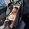baby, car_interior, car_seat, child, clothing, expression, face, hands, head, indoor, infant, person, portrait, safety, seat, seatbelt, sock, sunlight, vehicle, window