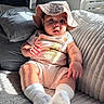 baby, child, infant, hat, romper, winnie_the_pooh, couch, pillows, window, sunlight, blinds, socks, striped_clothing, indoor, cute, curious, plush, seated, soft_lighting, face