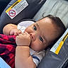 baby, infant, car_seat, blanket, red, black, checkered, hand, thumb, face, eyes, clothing, cute, child, sitting, indoors, warning_label, seat, portrait, young