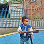 Divine Ntwayagae is registered to the contest to win money with this photo: blue_surface, brick_wall, casual_clothing, child, curious, daytime, fence, handlebar, jacket, outdoor, playground, pole, rusty, scooter, shorts, sidewalk, sneakers, toddler, tree, window