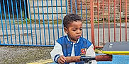 Divine Ntwayagae is registered to the contest to win money with this photo: blue_surface, brick_wall, casual_clothing, child, curious, daytime, fence, handlebar, jacket, outdoor, playground, pole, rusty, scooter, shorts, sidewalk, sneakers, toddler, tree, window