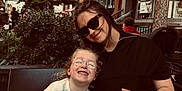 Mila-Rose is registered to the contest to win money with this photo: child, woman, glasses, sweater, striped_pants, outdoor, bench, smile, happy, tree, bush, tattoo_shop, building, street, sunglasses, person, casual, daytime, nature, portrait