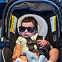 baby, sunglasses, car_seat, infant, blanket, clothing, child, seatbelt, indoor, person, cute, fashion, accessory, comfort, young, portrait, relaxed, toddler, soft_toy, casual