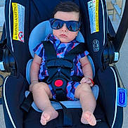 Jason is registered to the contest to win money with this photo: baby, car_seat, sunglasses, plaid_shirt, infant, child, outdoor, footwearless, seatbelt, serious_face, baby_boy, clothing, baby_accessory, sidewalk, door, plastic, fabric, sunlight, person, baby_fashion