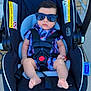 baby, car_seat, sunglasses, plaid_shirt, infant, child, outdoor, footwearless, seatbelt, serious_face, baby_boy, clothing, baby_accessory, sidewalk, door, plastic, fabric, sunlight, person, baby_fashion