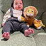 baby, infant, child, plush_toy, lion_toy, armchair, knit_pants, suspenders, cream_top, green_chair, soft_texture, indoor, cute, cozy, feet, face, portrait, seated, toy, curious_expression