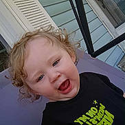 Chevelle joined the competition — help win amazing prizes! child, toddler, curly_hair, blue_eyes, black_shirt, text_on_clothing, outdoor, porch, door, house_siding, purple_chair, expression, happy, smiling, person, clothing, young_child, cute, casual, daylight