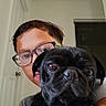 Nova joined the competition — help win amazing prizes! animal, black_dog, close_up, companion, curious, dog, door, face, glasses, holding, home, indoor, looking, person, pet, portrait, pug, short_hair, wall, young_person