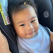 Keali'Inoa is registered to the contest to win money with this photo: baby, child, car_seat, bib, smile, face, infant, clothing, seatbelt, safety, cute, skin, hair, indoor, warning_label, human, young_child, portrait, seat, comfort