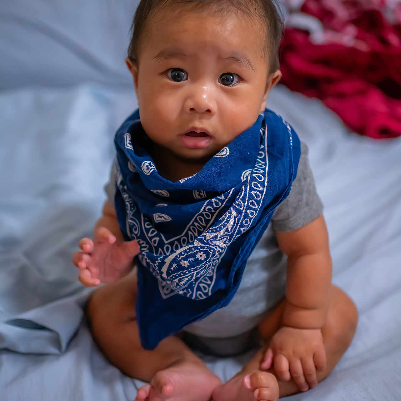 Keali'Inoa joined the competition — help win amazing prizes! baby, bandana, bed, blue_bandana, curious, expression, eyes, face, foot, hand, indoors, infant, looking_up, person, portrait, sitting, skin, toddler, wearing, young_child