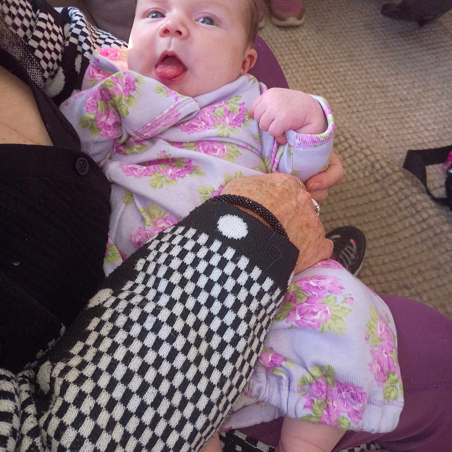 Susan is registered to the contest to win money with this photo: baby, blanket, carpet, checkered_pattern, child, cute, fabric, floral_clothing, footwear, hand, holding, indoor, infant, person, playful, purple, seated, skin, sleeve, tongue_out