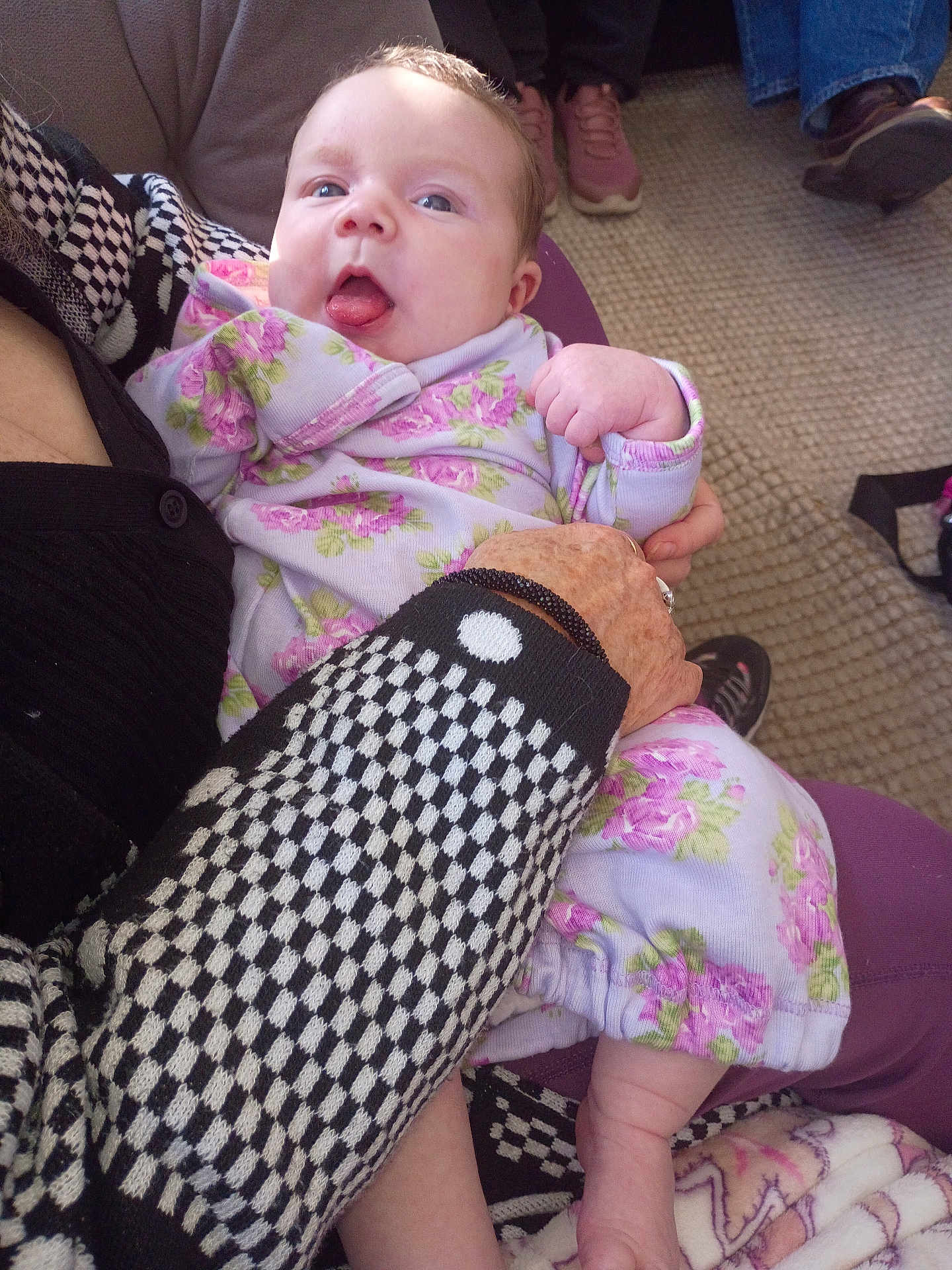 Susan is registered to the contest to win money with this photo: baby, infant, child, person, floral_clothing, purple, carpet, hand, sleeve, checkered_pattern, tongue_out, indoor, footwear, seated, holding, cute, playful, skin, fabric, blanket