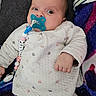 baby, beads, blanket, blue, clip, cozy, eyes, face, hand, indoor, infant, lying_down, onesie, pacifier, pacifier_chain, patterned_clothing, pillow, pink, soft_fabric, white