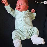 ézékiel participe au concours pour gagner de l'argent avec cette photo : baby, black_background, cable, clothing, cute, expressive, face, human, indoors, infant, lying_down, newborn, onesie, portrait, power_strip, raised_fist, resting, skin, small_hands, white_socks