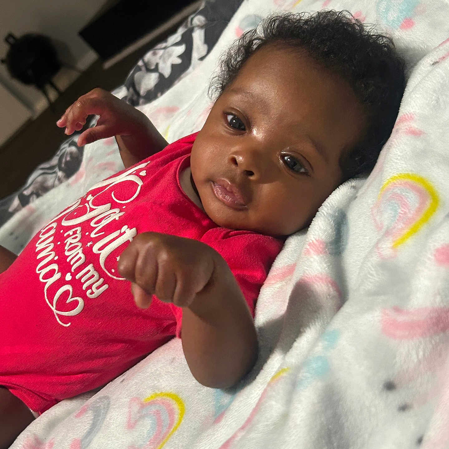 Niyari joined the competition — help win amazing prizes! baby, infant, blanket, red_clothing, rainbow_pattern, face, hand, lying_down, curious, indoors, soft_texture, cute, child, newborn, portrait, sleepwear, cozy, skin, head, young