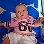 baby, child, infant, shirt, shorts, clothing, blue_chair, pattern, drool, face, eyes, arm, hand, sitting, indoor, cute, small_person, relaxing, looking_up, casual