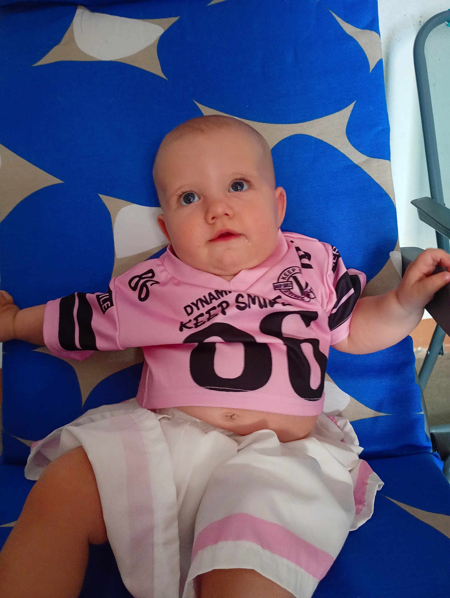 Juliette participe au concours pour gagner de l'argent avec cette photo : baby, child, infant, shirt, shorts, clothing, blue_chair, pattern, drool, face, eyes, arm, hand, sitting, indoor, cute, small_person, relaxing, looking_up, casual