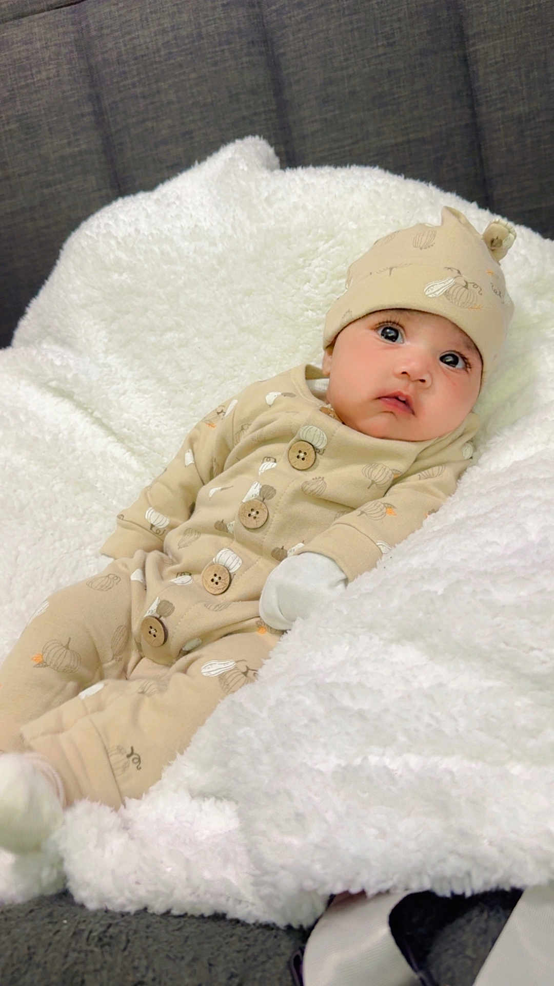 Sabreen joined the competition — help win amazing prizes! baby, infant, pajamas, hat, blanket, white_blanket, cozy, cute, indoors, portrait, child, soft_texture, sleepwear, seated, looking_up, warm_clothing, comfort, face, expression, small