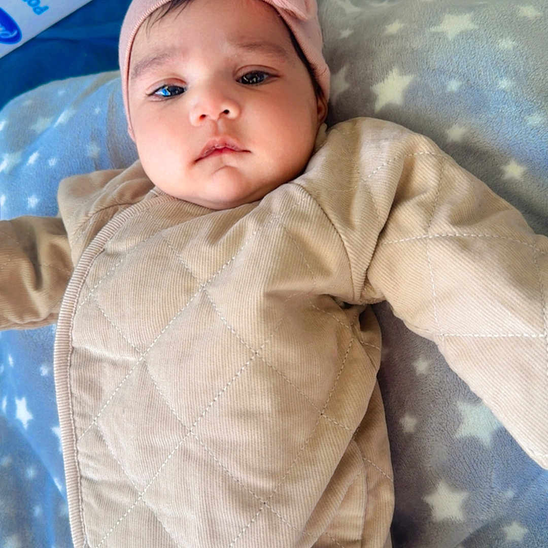 Sabreen is registered to the contest to win money with this photo: baby, beige, blanket, blue, box, child, curious, cute, face, headband, indoor, infant, lying_down, pink, portrait, quilted_clothing, soft_texture, star_pattern, toy_box, young
