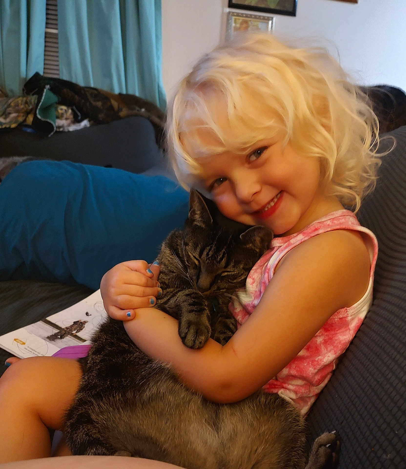 Allison joined the competition — help win amazing prizes! child, blonde_hair, smile, cat, tabby_cat, hugging, couch, indoor, cozy, happy, pet, person, sitting, book, curtain, furniture, home, nail_polish, tank_top, portrait