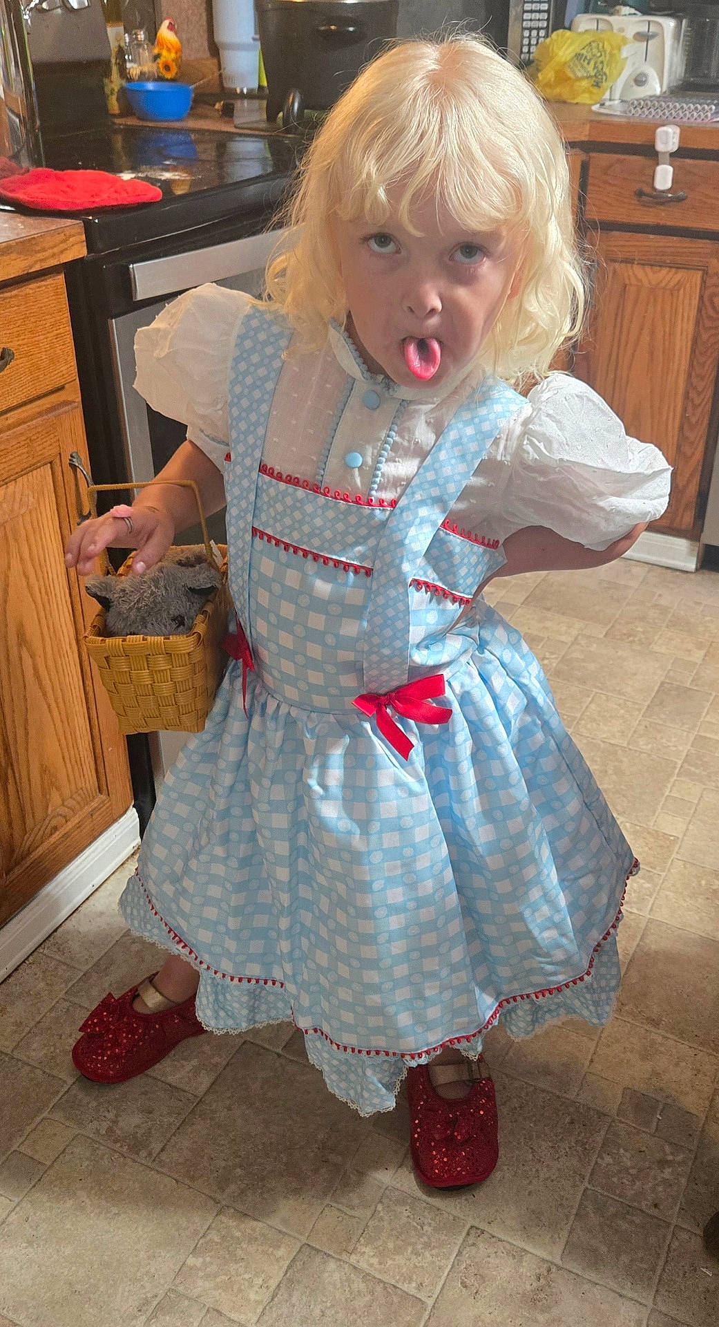 Allison joined the competition — help win amazing prizes! appliance, basket, blue, cabinet, child, cute, dress, floor, funny_face, indoor, kitchen, person, playful, red_bows, sparkly_shoes, standing, stuffed_animal, tongue_out, white, wooden_cabinet